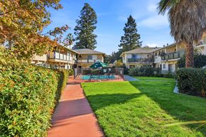 Sunnyvale apartment for rent - A pathway leads through a grassy area with a tennis court and apartment buildings in the background.