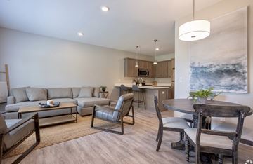 West Olive townhouse for rent - A modern living room with a grey sofa, a wooden dining table and chairs, and a kitchen area in the background.