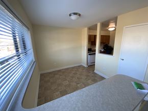 Silver Spring apartment for rent - A bedroom with a bed, a window with blinds, and a kitchen area in the background.