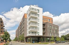 Alexandria apartment for rent - A modern multi-story building with a white and brown facade is situated on a street corner with cars parked in front.