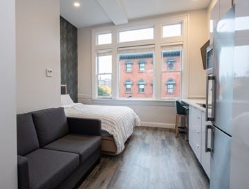 Providence apartment for rent - A grey couch sits in a living room with a window overlooking a red brick building.