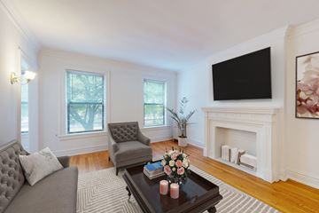 Chicago apartment for rent - A living room with a grey couch, a grey armchair, a coffee table with flowers and candles, a fireplace, and a flat screen TV mounted on the wall.