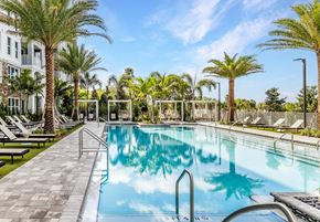 West Palm apartment for rent - A swimming pool surrounded by palm trees and lounge chairs.