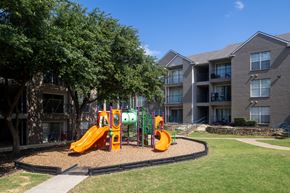 Carrollton apartment for rent - A playground with a slide and a climbing frame in front of apartment buildings.