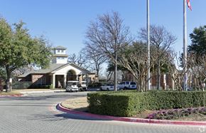 Euless apartment for rent - A building with a tower and a flag on top is surrounded by trees and has a driveway leading to it.
