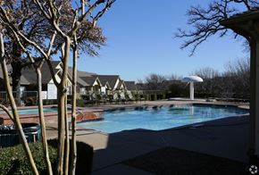 Euless apartment for rent - A pool surrounded by trees and a building in the background.
