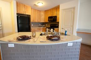Waco apartment for rent - A kitchen with a black fridge and microwave, a white counter top, and wooden cabinets.