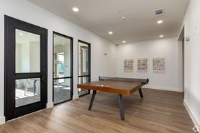 Plano apartment for rent - A pool table is in the middle of a room with a black door and a white wall.