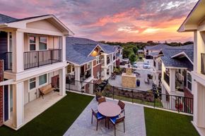 Fort Worth apartment for rent - A sunset view from a balcony overlooking a courtyard with a table and chairs.