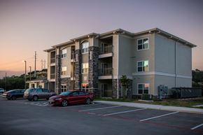Kerrville apartment for rent - A red car is parked in a parking lot in front of a building.