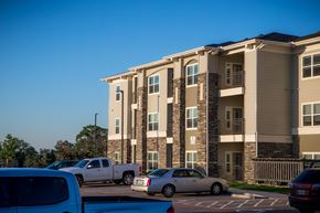 Kerrville apartment for rent - A row of cars are parked in a parking lot in front of a large apartment building.