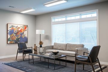 Kerrville apartment for rent - A living room with a grey couch, a black chair, a glass table, and a painting on the wall.