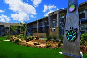 Denton apartment for rent - A large wooden pole with a colorful design stands in front of a building with a green lawn and trees.