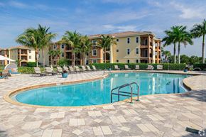 Fort Myers apartment for rent - A swimming pool surrounded by a brick patio and palm trees in front of apartment buildings.