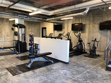 Omaha apartment for rent - A gym with a variety of equipment including a bench, weights, and a television.