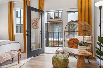 Omaha apartment for rent - A living room with a white sofa, a wicker chair, a round ottoman, and a table with a pumpkin on it.