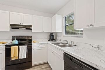 Tampa townhouse for rent - a kitchen with white cabinets and black appliances and a window