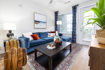Jacksonville apartment for rent - A living room with a blue couch, a wooden coffee table, and a painting on the wall.
