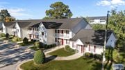 Greenville apartment for rent - A white building with red doors and windows is surrounded by greenery.