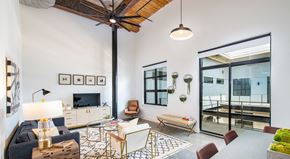Greenville apartment for rent - A living room with a dark blue sofa, a wooden coffee table, and a TV on the wall at Judson Mill Lofts and The Jenny & Westervelt in Greenville, SC
