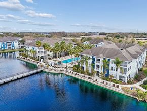 Tampa apartment for rent - A large white building with a pool is surrounded by palm trees and a body of water.