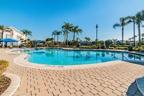 Brandon apartment for rent - Apartments Near Downtown Tampa, FL - 2211 Grand Isle - Pool Area with Stone Tile Ground, Poolside Seating and Umbrellas, with Surrounding Trees and Greenery in the Background