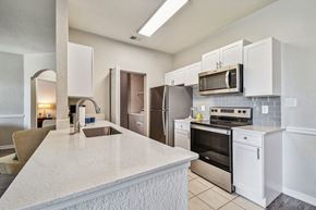Brandon apartment for rent - Four BR Apartments in Brandon FL - 2211 Grand Isle - Modern Aisle-Style Kitchen with Stainless Steel Appliances, White Cabinetry, Grey Tile Backsplash, Overhead White Lighting, with View of Washer/Dryer Facilities