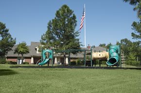 Little Rock apartment for rent - A playground with a green slide and a yellow slide in front of a house with an American flag.