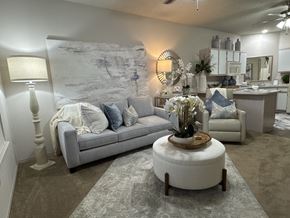 Bryant apartment for rent - A living room with a grey couch, a round ottoman, and a large mirror on the wall.