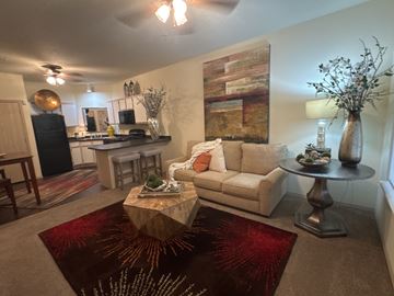 Bryant apartment for rent - A living room with a white couch, a wooden coffee table, and a large abstract painting on the wall.