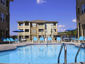 Fayetteville apartment for rent - a swimming pool with blue chairs and a building in the background