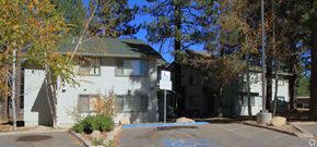South Lake Tahoe apartment for rent - A white building with a green roof is surrounded by trees.