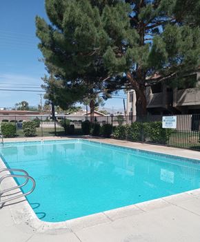 Las Vegas apartment for rent - A pool surrounded by trees and a fence with a sign on it.