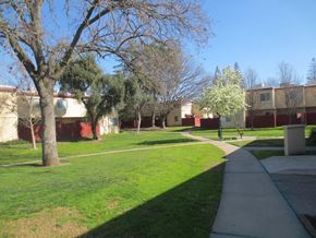 Sacramento townhouse for rent - Large lawn with trees and concrete walkway with red fencing at American River Gardens, Sacramento