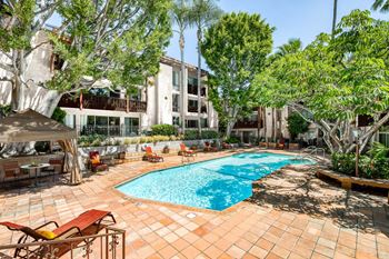 A pool surrounded by trees and chairs.