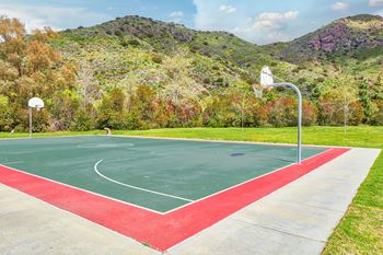 A basketball court with a red and green surface and a mountain in the background.