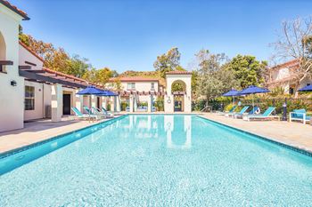 A swimming pool with chairs and umbrellas next to a house