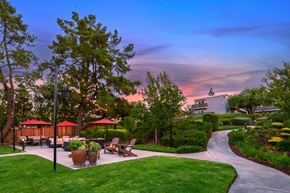 Pleasanton apartment for rent - A beautiful outdoor seating area with tables and chairs surrounded by greenery and trees.