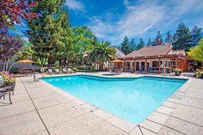 Pleasanton apartment for rent - A large swimming pool surrounded by trees and a house in the background at Valley Plaza Villages, California, 94566
