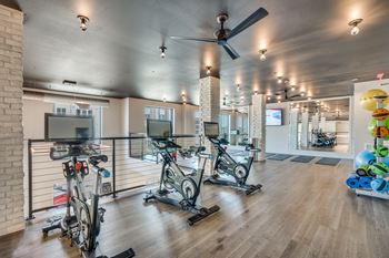 A gym with a row of exercise bikes and a fan.