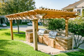 A wooden pergola with two brick barbecue pits in a yard