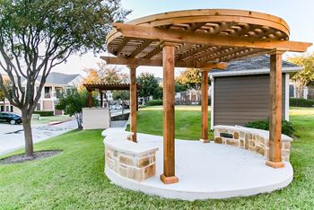 A patio with a stone table and a wooden pavilion in a yard