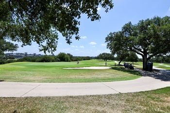 A golf course in a park with trees and a sidewalk