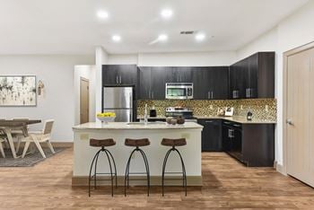 A kitchen with black cabinets and a counter top with three stools