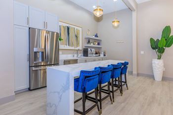 A kitchen with a long island with blue chairs and a stainless steel refrigerator