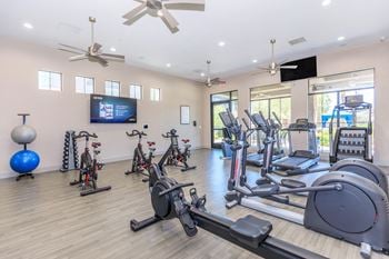 A gym with cardio machines and weights and a tv