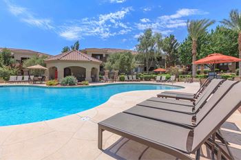 A swimming pool with chairs and umbrellas in front of a house