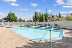 Olympia apartment for rent - A large swimming pool surrounded by a white fence and blue lounge chairs at Abbey Rowe Apartments in Olympia, WA