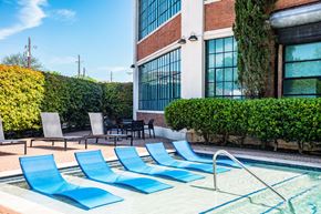 Dallas apartment for rent - a swimming pool with blue lounge chairs in front of a building