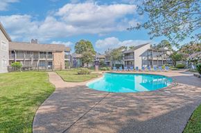 Shreveport apartment for rent - A swimming pool with a walkway and grassy area with apartment buildings in the background at Laurel Parc apartments in Shreveport, LA.